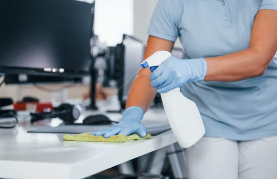 Close up view of woman in protective gloves that cleaning tables in the office.
