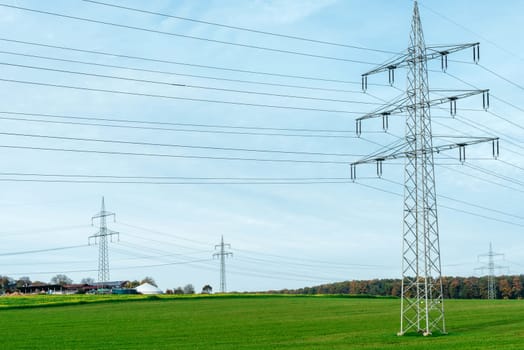 High voltage power lines leading through a green field. Transmission of electricity by means of supports through agricultural areas.