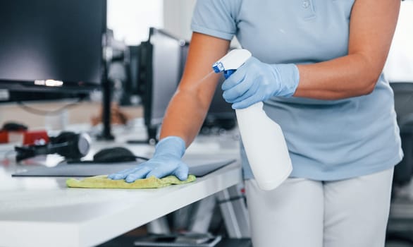 Close up view of woman in protective gloves that cleaning tables in the office.