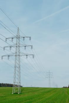 High voltage power lines leading through a green field. Transmission of electricity by means of supports through agricultural areas.