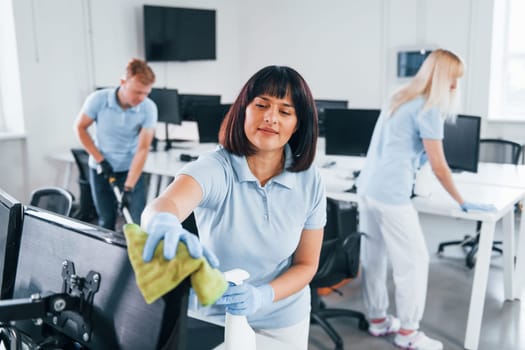 Cleans monitor. Group of workers clean modern office together at daytime.