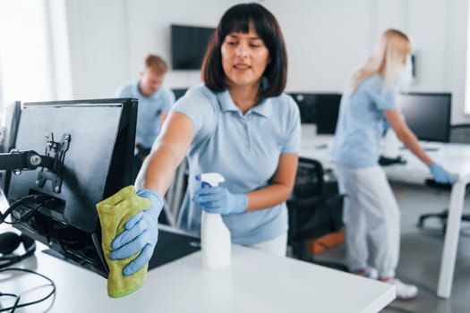 Cleans monitor. Group of workers clean modern office together at daytime.