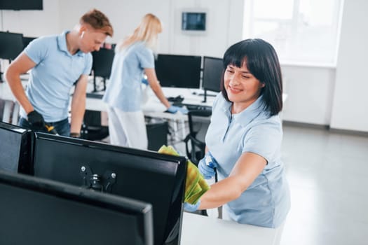 Cleans monitor. Group of workers clean modern office together at daytime.