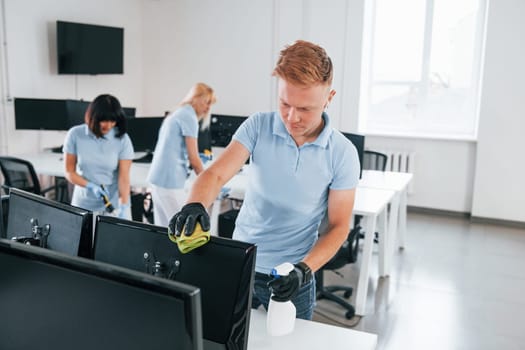 Cleans monitor. Group of workers clean modern office together at daytime.