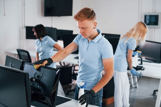 Cleans monitor. Group of workers clean modern office together at daytime.