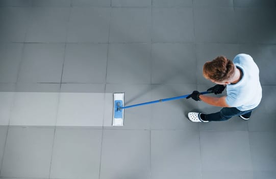 Top view of man in blue shirt and protective gloves that uses vacuum cleaner.