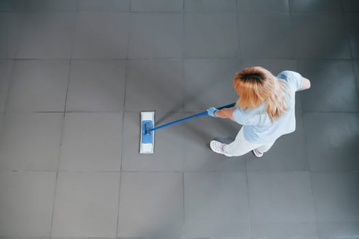 Top view of woman in blue shirt and protective gloves that uses vacuum cleaner.