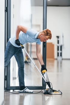 Young man works in the modern office. Uses vacuum cleaner.