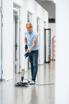 Young man works in the modern office. Uses vacuum cleaner.