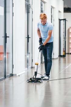Young man works in the modern office. Uses vacuum cleaner.