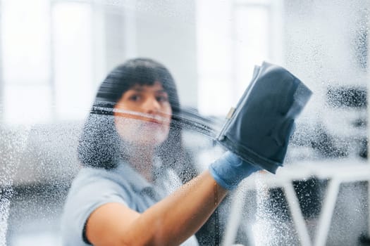 Woman cleaning dirty window by using towel. View through the glass.