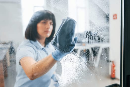 Woman cleaning dirty window by using towel. View through the glass.