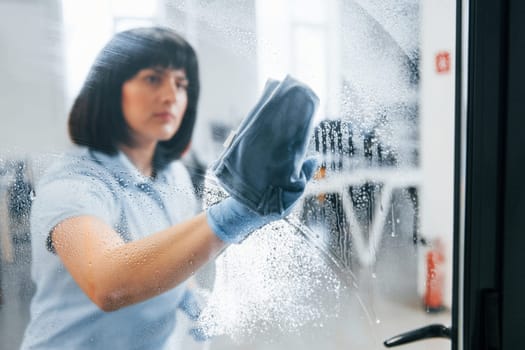 Woman cleaning dirty window by using towel. View through the glass.