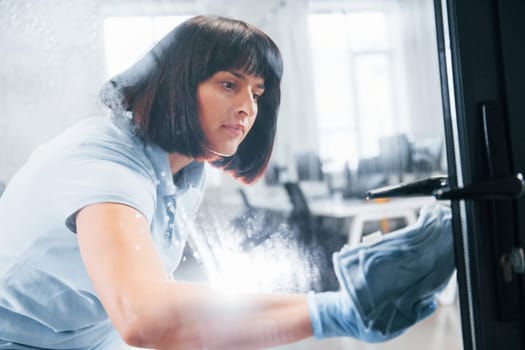 Woman cleaning dirty window by using towel. View through the glass.