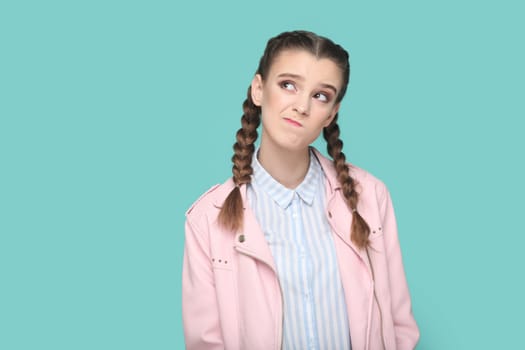 Portrait of pensive thoughtful young teenager girl with braids wearing pink jacket looking away with puzzled confused expression. Indoor studio shot isolated on green background.