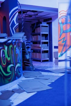 Urban graffiti artwork glowing under neon lights in deserted messy warehouse, empty building filled with spray paint and garbage, fluorescent bright blue light. Abandoned damaged space.