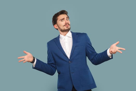 Portrait of confused puzzled man with mustache standing with spread hands asking what with uncertain angry expression wearing official style suit. Indoor studio shot isolated on light blue background.
