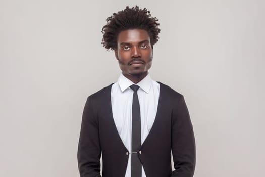 Attractive serious man with petit goatee looking at camera with confident and thoughtful expression on his face, wearing white shirt and tuxedo. Indoor studio shot isolated on gray background.