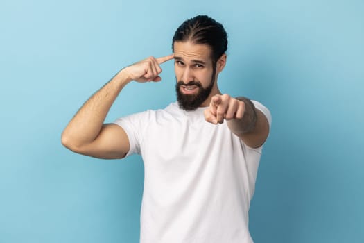 You are nuts. Portrait of man with beard showing stupid gesture and pointing to camera, accusing dumb insane suggestion, crazy plan for idiots. Indoor studio shot isolated on blue background.