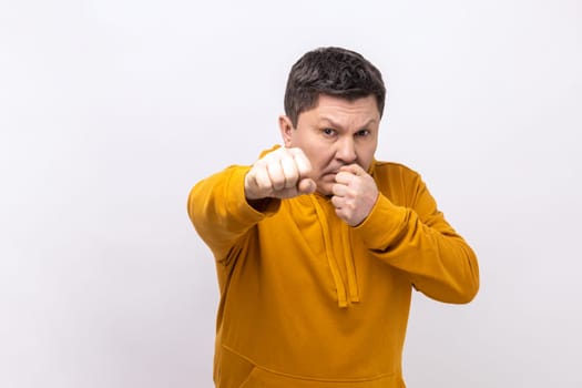 Portrait serious aggressive man holding clenched fists up ready to boxing, defending his rights and freedom, wearing urban style hoodie. Indoor studio shot isolated on white background.