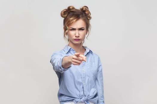 You are guilty in my misfortune. Displeased blonde woman blaming someone, pointing directly at camera, making serious face, wearing blue shirt. Indoor studio shot isolated on gray background.