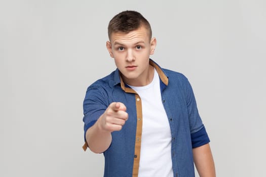 Are you ready. Portrait of handsome teenager boy wearing blue shirt pointing finger at camera choosing you, scolding and forcing to move on. Indoor studio shot isolated on gray background.