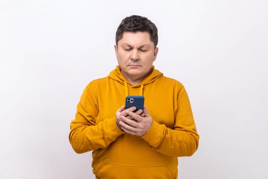 Portrait of concentrated middle aged man texting message in social media on cell phone, using mobile network services, wearing urban style hoodie. Indoor studio shot isolated on white background.