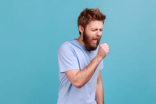 Portrait of unhealthy sick bearded man have cough and feeling pain in his lungs, has symptoms of influenza, having high temperature. Indoor studio shot isolated on blue background.