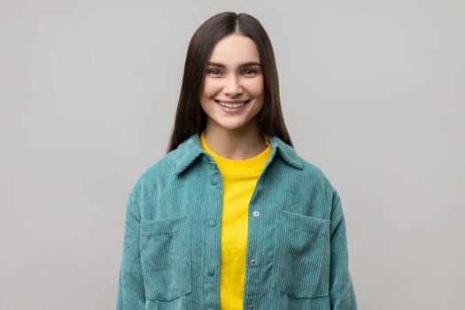 Portrait of happy successful young woman standing looking at camera with charming and joyous toothy smile, wearing casual style jacket. Indoor studio shot isolated on gray background.