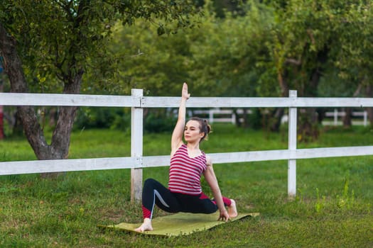 Full length of motivated fit athletic woman wearing sportswear practicing yoga on mat outdoor in summer day, standing in Virabhadrasana warrior pose and meditating, doing stretching exercise.