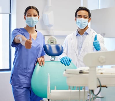 Well give you a smile thats brighter than before. Portrait of two young dentists showing thumbs up in their consulting room