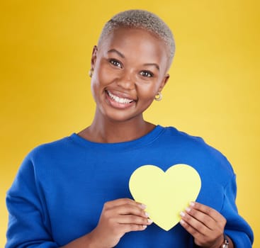 Paper heart, portrait and happy black woman in studio, background and color backdrop. Smile, female model and yellow shape for love, wellness and caring support of peace, romance and sign of kindness.