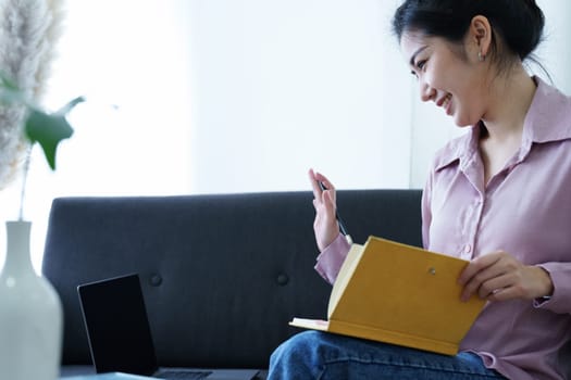 Portrait of a self-employed Asian woman holding a notebook and using a computer doing video conference at home.