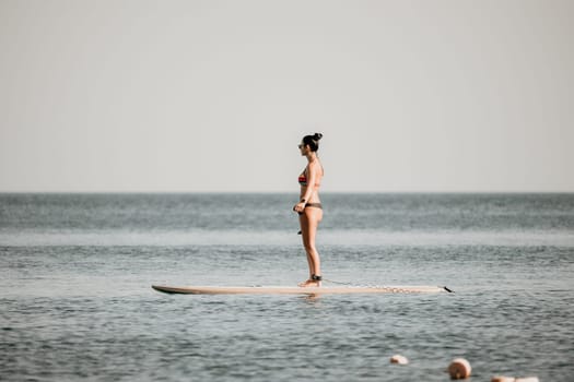 Sea woman sup. Silhouette of happy middle aged woman in rainbow bikini, surfing on SUP board, confident paddling through water surface. Idyllic sunset. Active lifestyle at sea or river