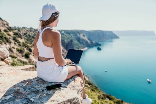 Digital nomad, Business woman working on laptop by the sea. Pretty lady typing on computer by the sea at sunset, makes a business transaction online from a distance. Freelance remote work on vacation