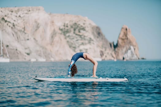 Woman sup yoga. Middle age sporty woman practising yoga pilates on paddle sup surfboard. Female stretching doing workout on sea water. Modern individual hipster outdoor summer sport activity