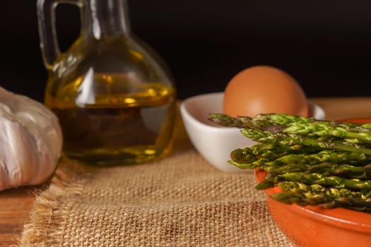 close-up of wild asparagus in an earthenware casserole with olive oil, eggs and garlic black background