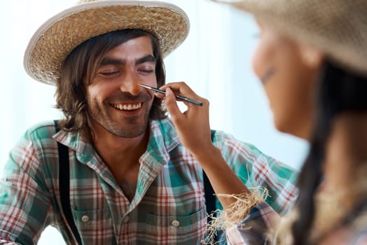 Does that tickle. a young woman applying makeup to a young man at home