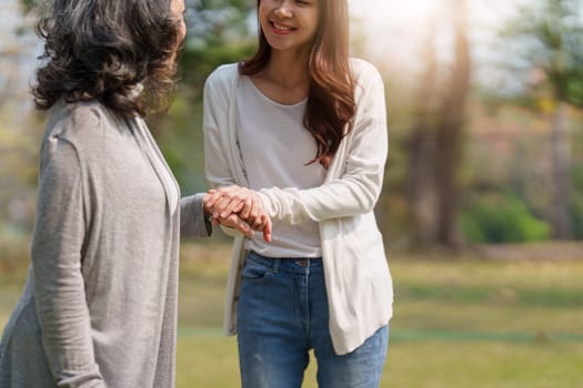 Close up of Adult daughter holding her elderly mother hand with love and walk together.