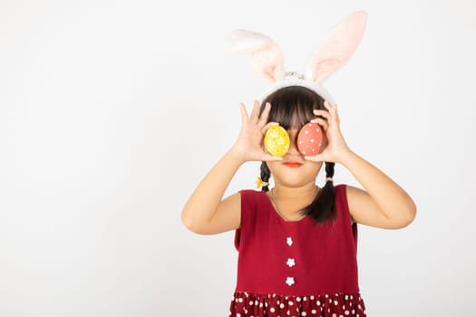 Happy Easter Day. Smile Asian little girl wearing easter bunny ears holding colorfull eggs closes eyes with testicles isolated on white background with copy space, Happy child in holiday