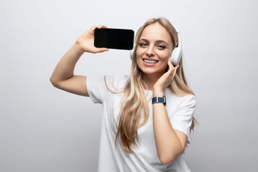 girl in wireless headphones with a smartphone mockup in her hands on a white background.