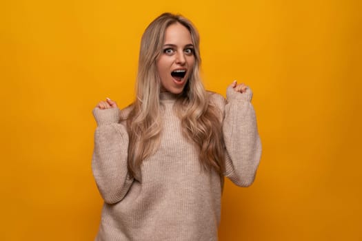 horizontal photo of a blonde young woman screaming on a yellow background.