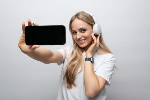 girl in wireless headphones with a smartphone mockup in her hands on a white background.