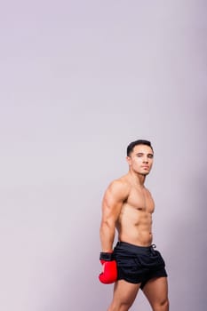 Muscular model sports young man in a boxing gloves on grey background. Male flexing his muscles.