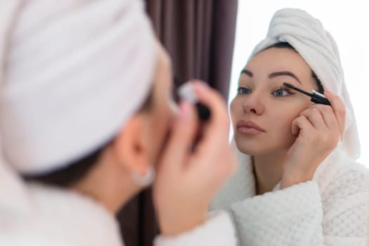 A woman applies black mascara to her eyelashes with a makeup brush. Young beautiful woman applying mascara makeup on her eyes in the bathroom.