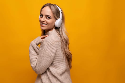 girl grimaces with big headphones in a studio with a yellow background.