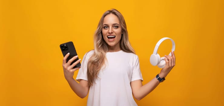 girl with a smartphone and headphones in her hands on an orange background.