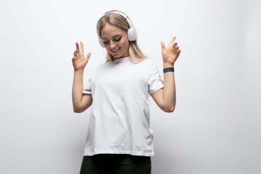 student girl listening to music with wireless headphones in a studio with white walls.