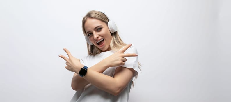 young woman having fun with music with wireless headphones in a studio with white walls.