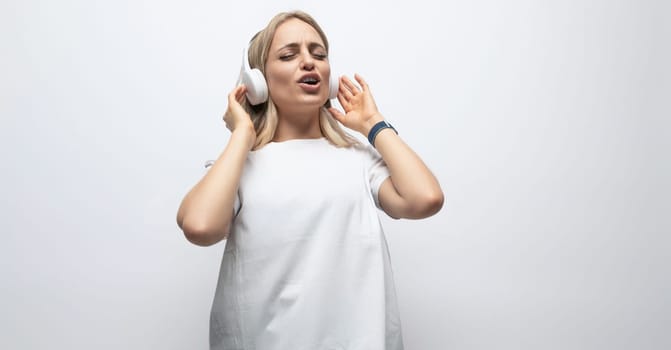 young woman having fun with music with wireless headphones in a studio with white walls.